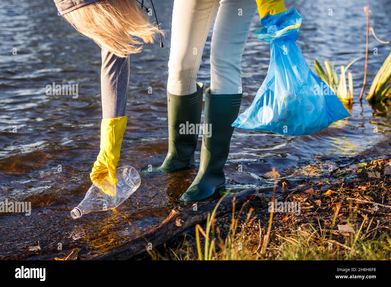 Volontario che raccoglie la bottiglia di plastica da lago o fiume inquinato. Danni ambientali. Inquinamento idrico con rifiuti di plastica Foto Stock