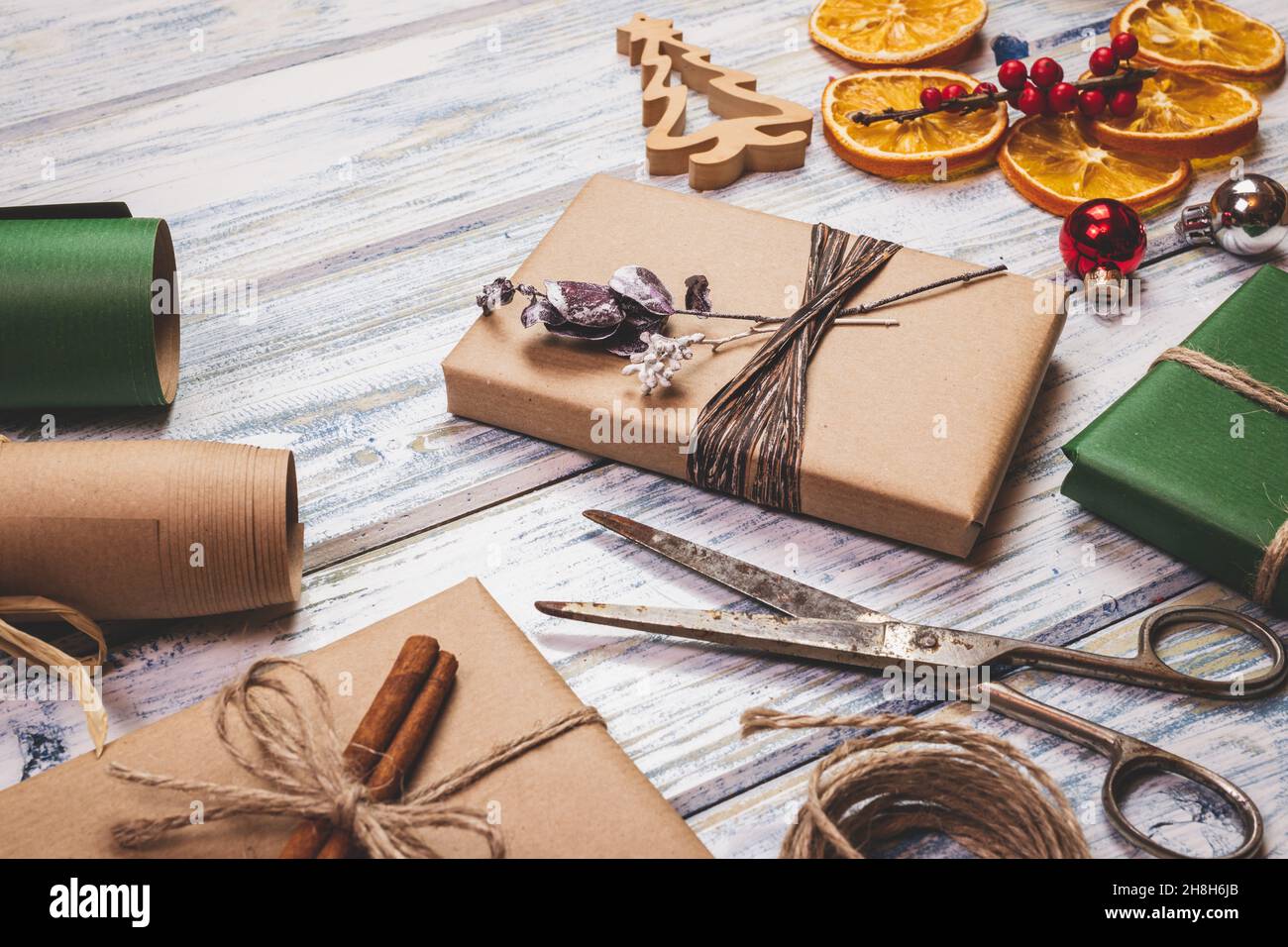 Preparazione delle confezioni regalo per Natale. Decorazione e regalo di natale avvolto su tavola di legno. Carta da imballaggio, forbici e ornamenti di festa Foto Stock