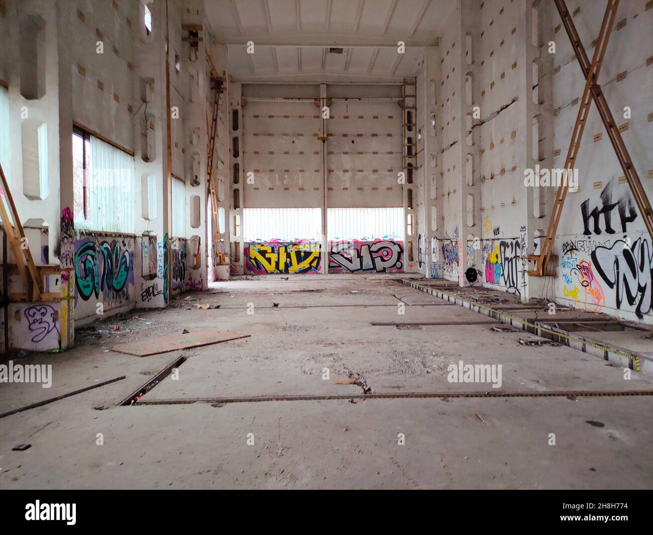 Grande magazzino vuoto abbandonato interno. Segnature sul muro con vernici a spruzzo colorate. Cartone sul pavimento. Interno del magazzino con pareti bianche. Stanza della fabbrica. Loft vuoto. Foto Stock
