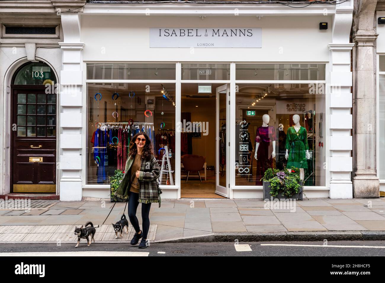 Una donna ben vestita cammina i suoi cani oltre il negozio di abbigliamento femminile Isabel Manns, Marylebone High Street, Londra, Regno Unito. Foto Stock