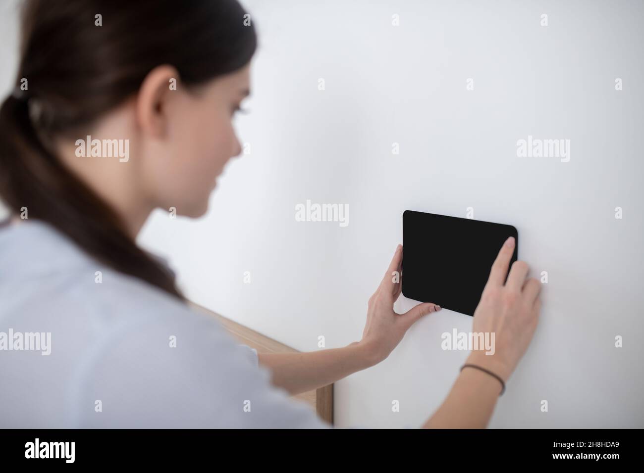 Donna con un ponytail che fissa un gadget alla superficie verticale Foto Stock