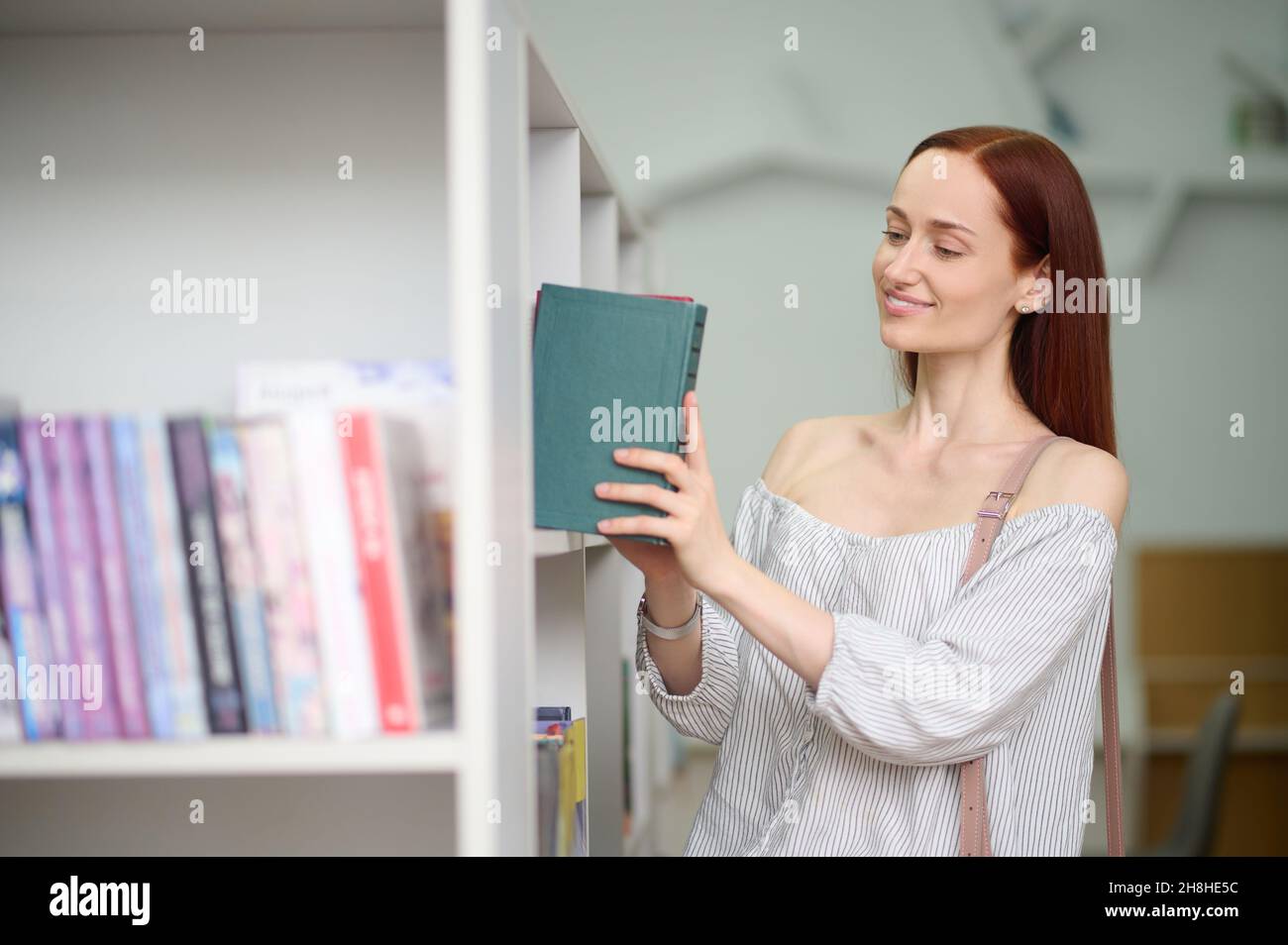 Donna che mette il libro in scaffale in biblioteca Foto Stock