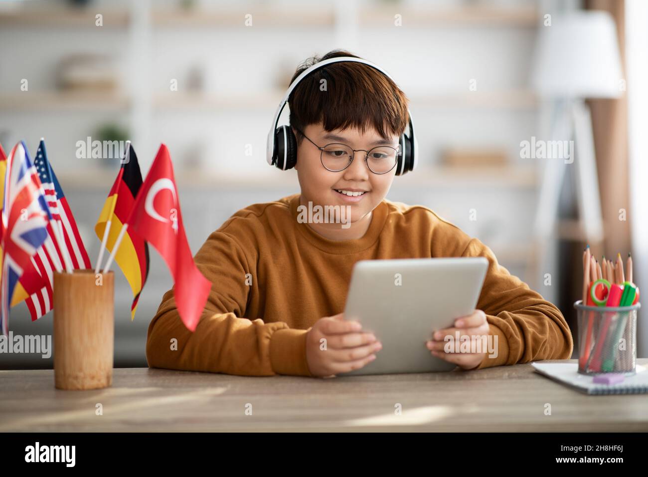 Felice ragazzo asiatico chubby utilizzando tablet digitale e cuffie wireless Foto Stock