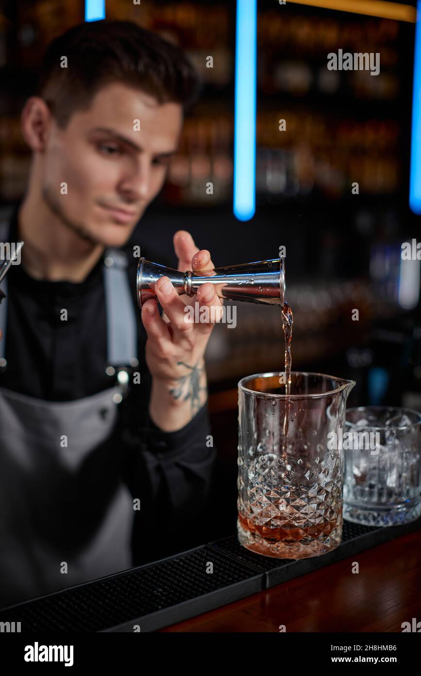 Barman in grembiule aggiunge l'ingrediente al vetro Foto Stock