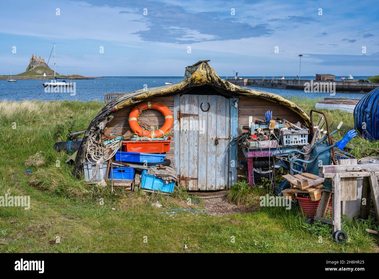 Imbarcazione capovolta utilizzata come capanna sulla spiaggia con vista distante del Castello di Lindisfarne sulla costa del Northumberland d'Inghilterra, Regno Unito Foto Stock
