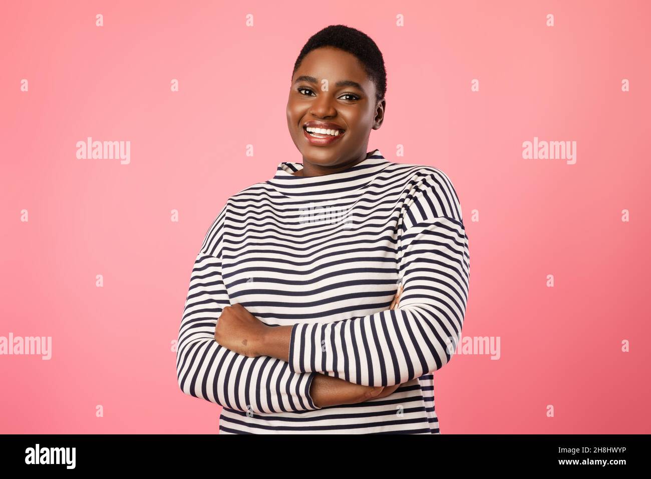 Donna africana sovrappeso con taglio corto che posa su sfondo rosa Foto Stock