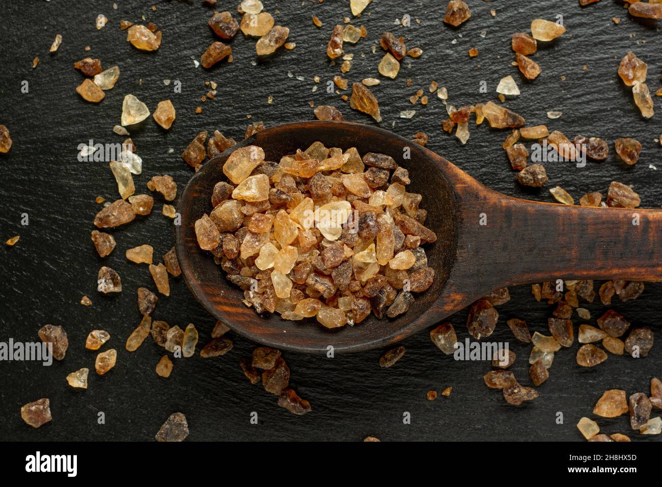 Cucchiaio di legno pieno di zucchero semolato marrone scuro su sfondo ardesia da vicino. Foto Stock