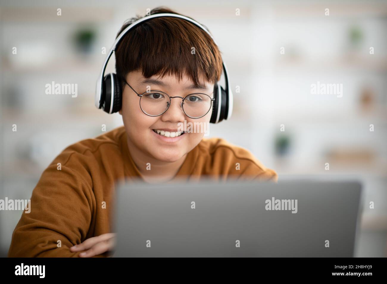 Ritratto closeup di ragazzo asiatico allegro utilizzando laptop e cuffie Foto Stock
