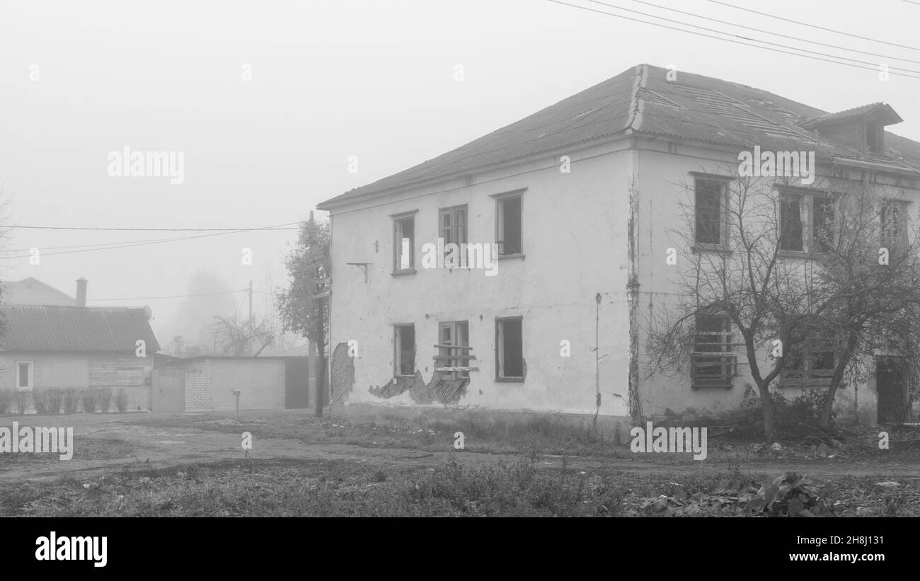 Una casa in legno abbandonata a due piani sulla strada in un giorno di nebbia, foto in bianco e nero Foto Stock