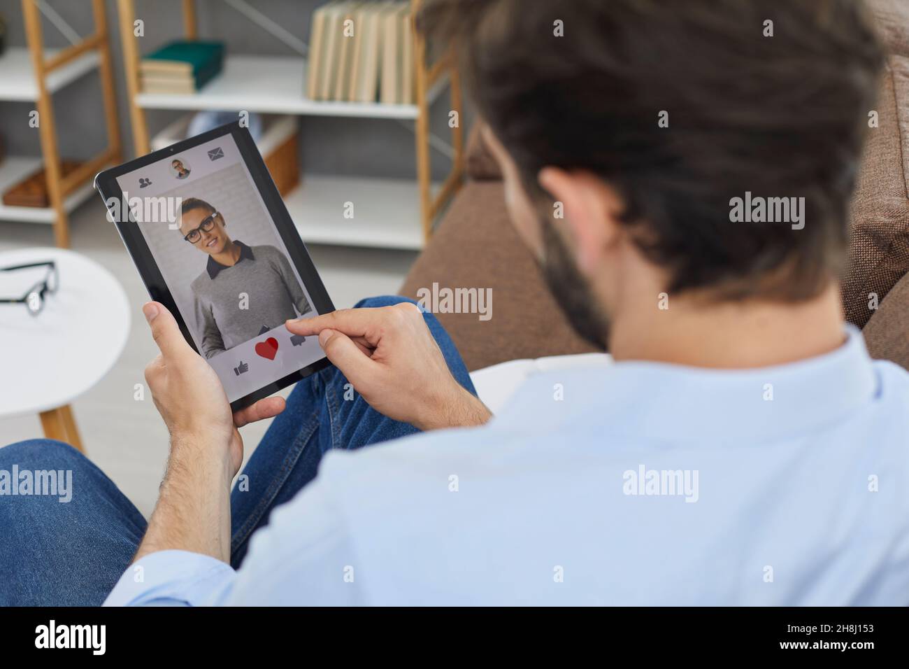 L'uomo sul tablet digitale guarda la foto del profilo di una giovane donna attraente nell'app dating. Foto Stock