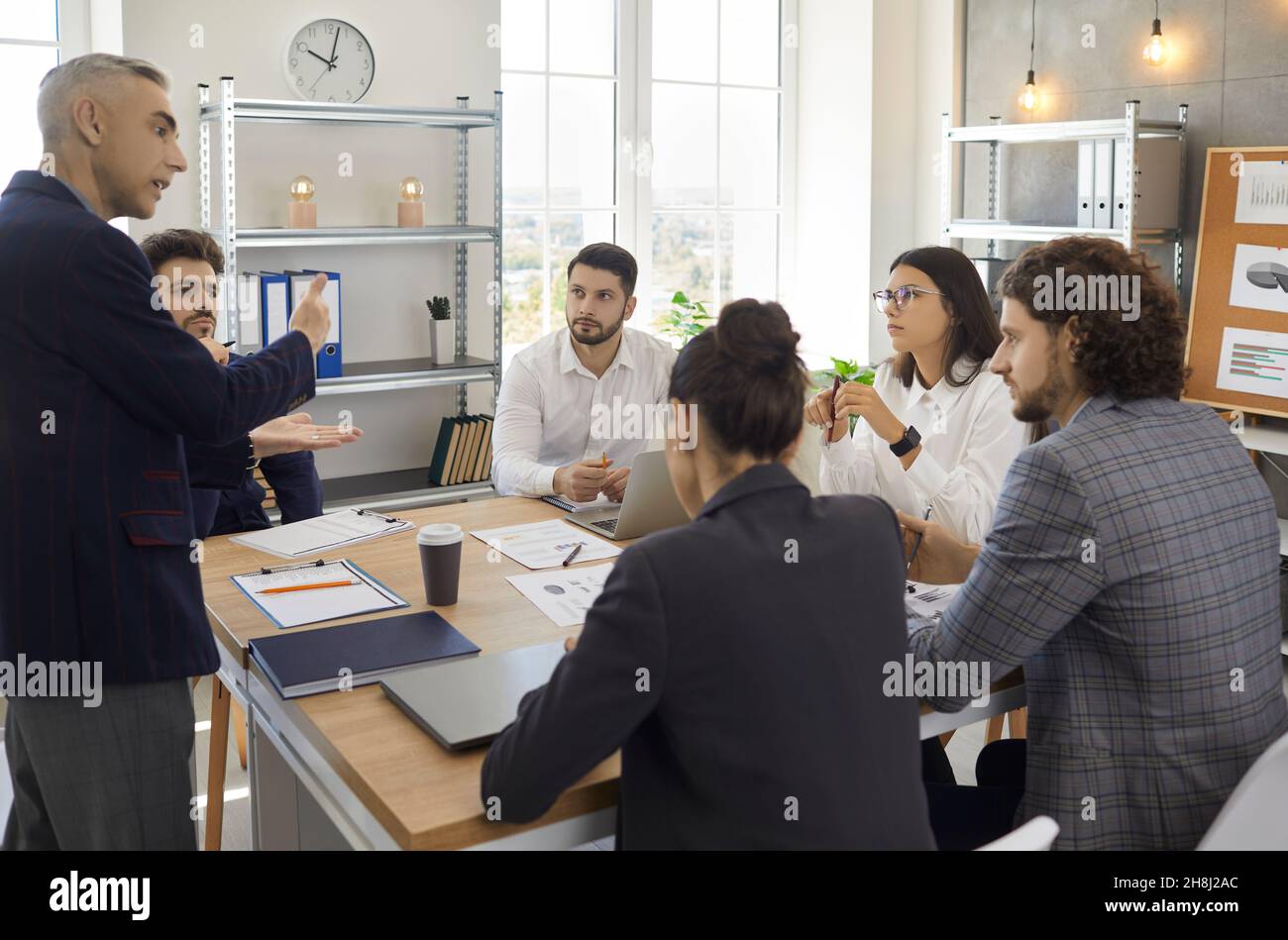 Il Senior Manager istruisce i giovani dipendenti in una riunione aziendale a un tavolo in un ufficio moderno. Foto Stock