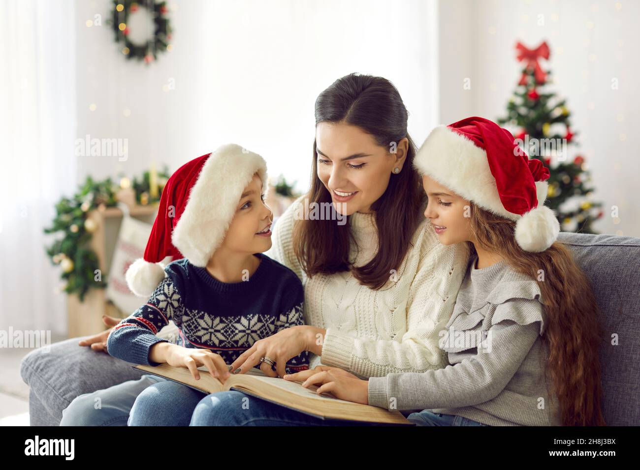 Felice madre e bambini seduti sul divano e libro di lettura la vigilia di Natale a casa Foto Stock