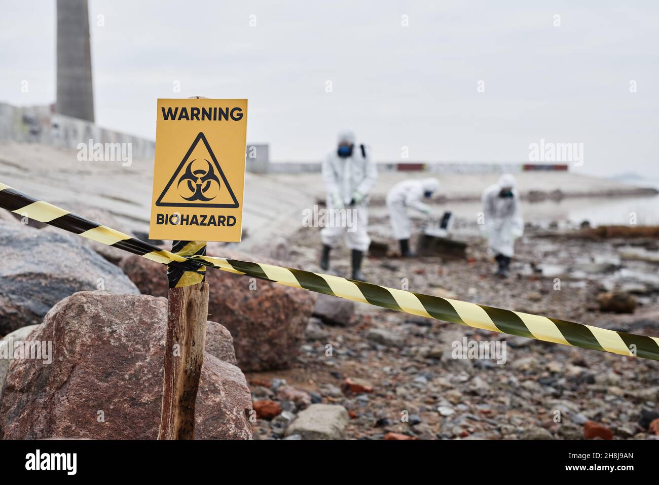 Primo piano del cartello di avvertimento pericolo biologico presso il sito di disastro ecologico con persone in tute protettive, spazio copia Foto Stock