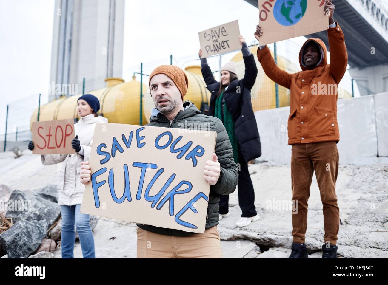 Un gruppo diversificato di persone che tiene cartelli e grida protestando nel sito di disastro ambientale, spazio copia Foto Stock