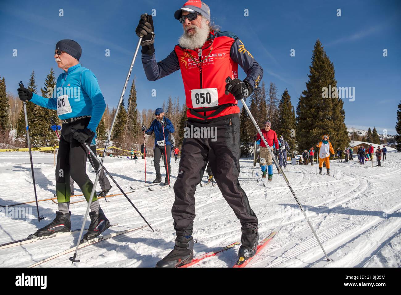 Primo piano di due atleti maschi di livello superiore sugli sci di fondo che corrono attraverso la linea di partenza del Chama Chile Ski Classic, altri piloti in lontananza. Foto Stock