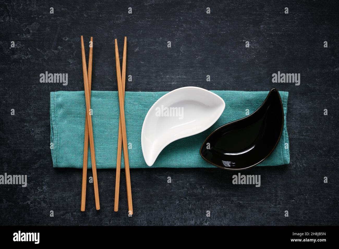 Ciotole e bacchette in ceramica bianca e nera adagiate su tovagliolo di lino, sfondo scuro, vista dall'alto Foto Stock