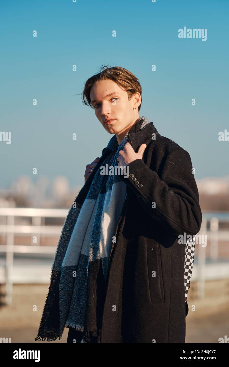 Giovane uomo in vecchio cappotto di lana, sciarpa e pantaloni corti si erge  di profilo in città impostazione Foto stock - Alamy