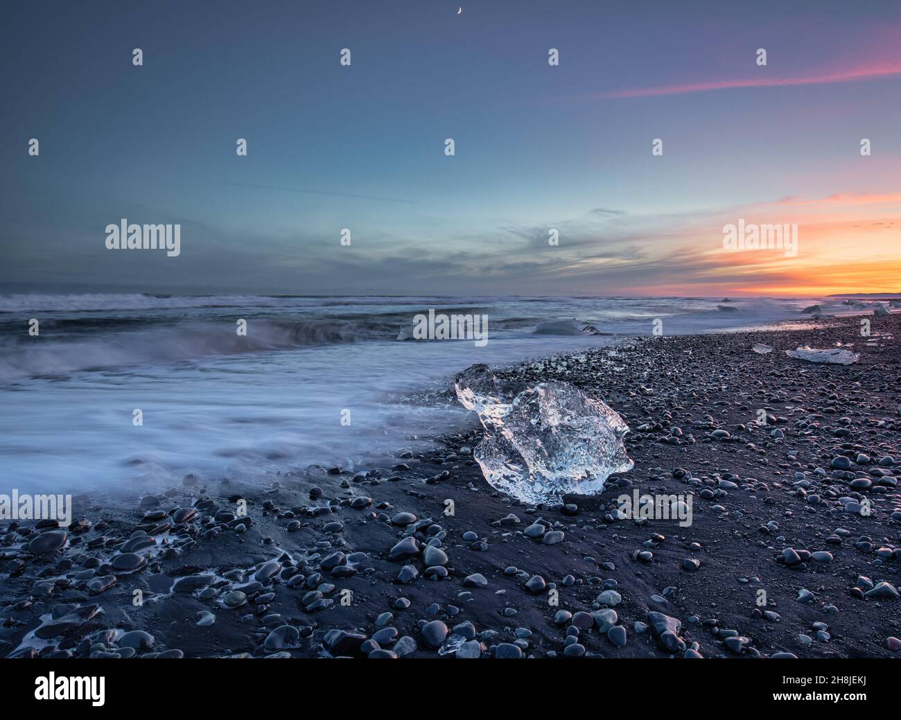 Un pezzo unico di ghiaccio sulla famosa spiaggia nera di Jokulsarlon, Islanda, durante il tramonto. Foto Stock