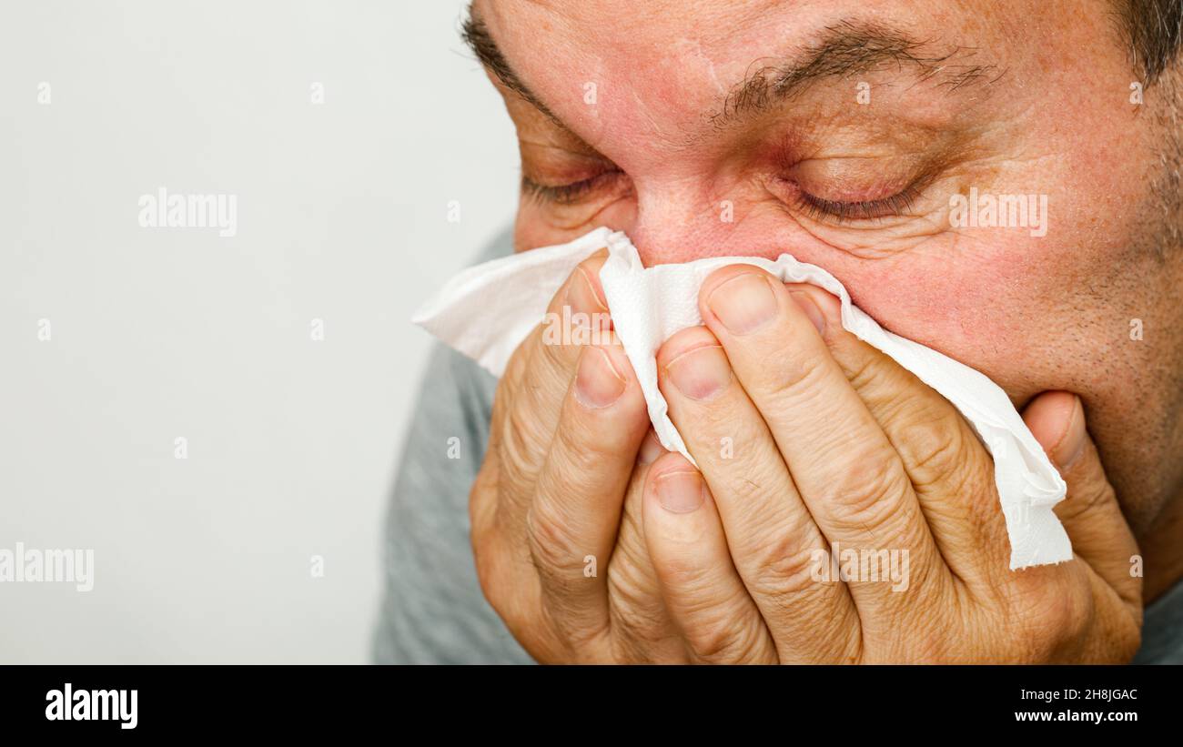 Un uomo ha un freddo e soffia il naso in un fazzoletto Foto Stock
