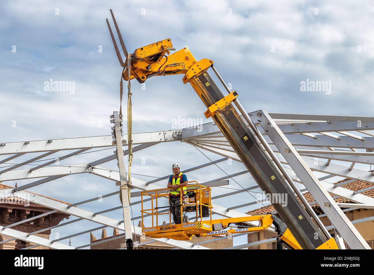 Barcellona, Spagna - 22 settembre 2021: Un lavoratore sta montando la cornice metallica di una tenda per eventi su una piattaforma di sollevamento Foto Stock