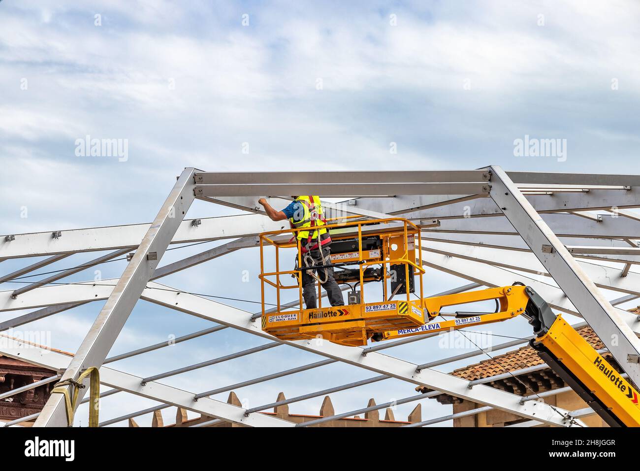Barcellona, Spagna - 22 settembre 2021: Un lavoratore sta montando la cornice metallica di una tenda per eventi su una piattaforma di sollevamento Foto Stock