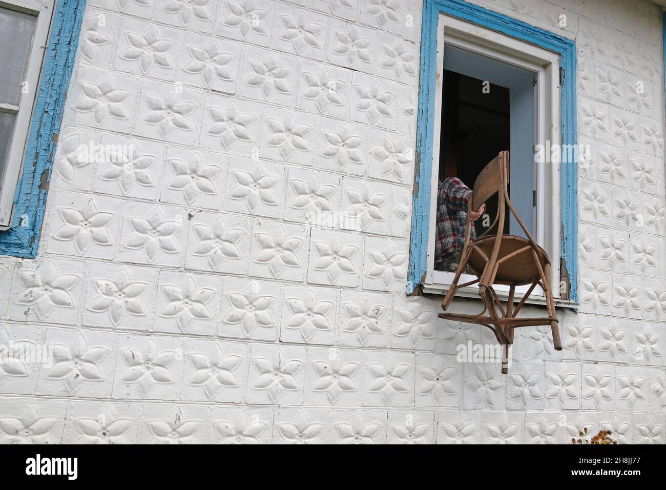 Un uomo getta una vecchia sedia fuori dalla finestra Foto Stock