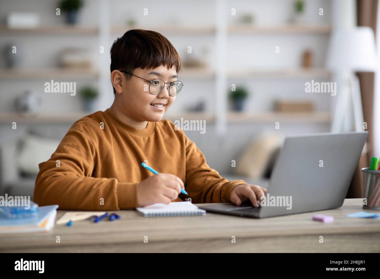 Ragazzo asiatico intelligente seduto di fronte al computer portatile, facendo i compiti Foto Stock