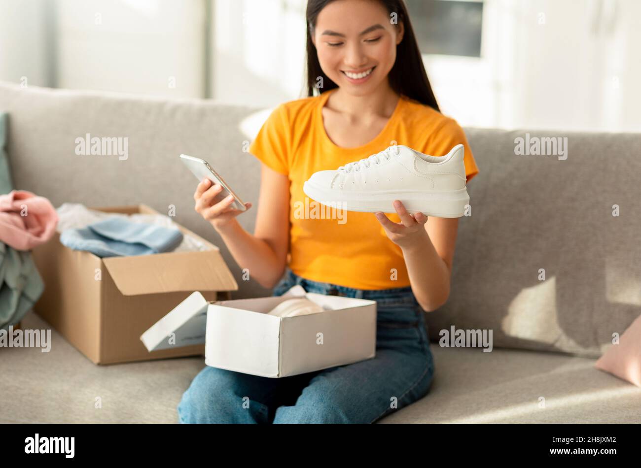 Donna asiatica positiva disimballaggio pacco con nuove scarpe sportive e  tenere smartphone, scrivendo online negozio feedback Foto stock - Alamy