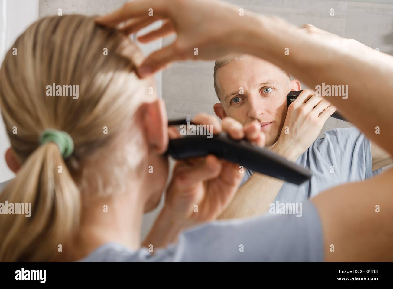L'uomo che rasa i capelli da solo, auto taglio a casa di fronte allo  specchio in bagno. Maschio con taglio lungo utilizzando il rifinitore della  macchina da rasatura Foto stock - Alamy