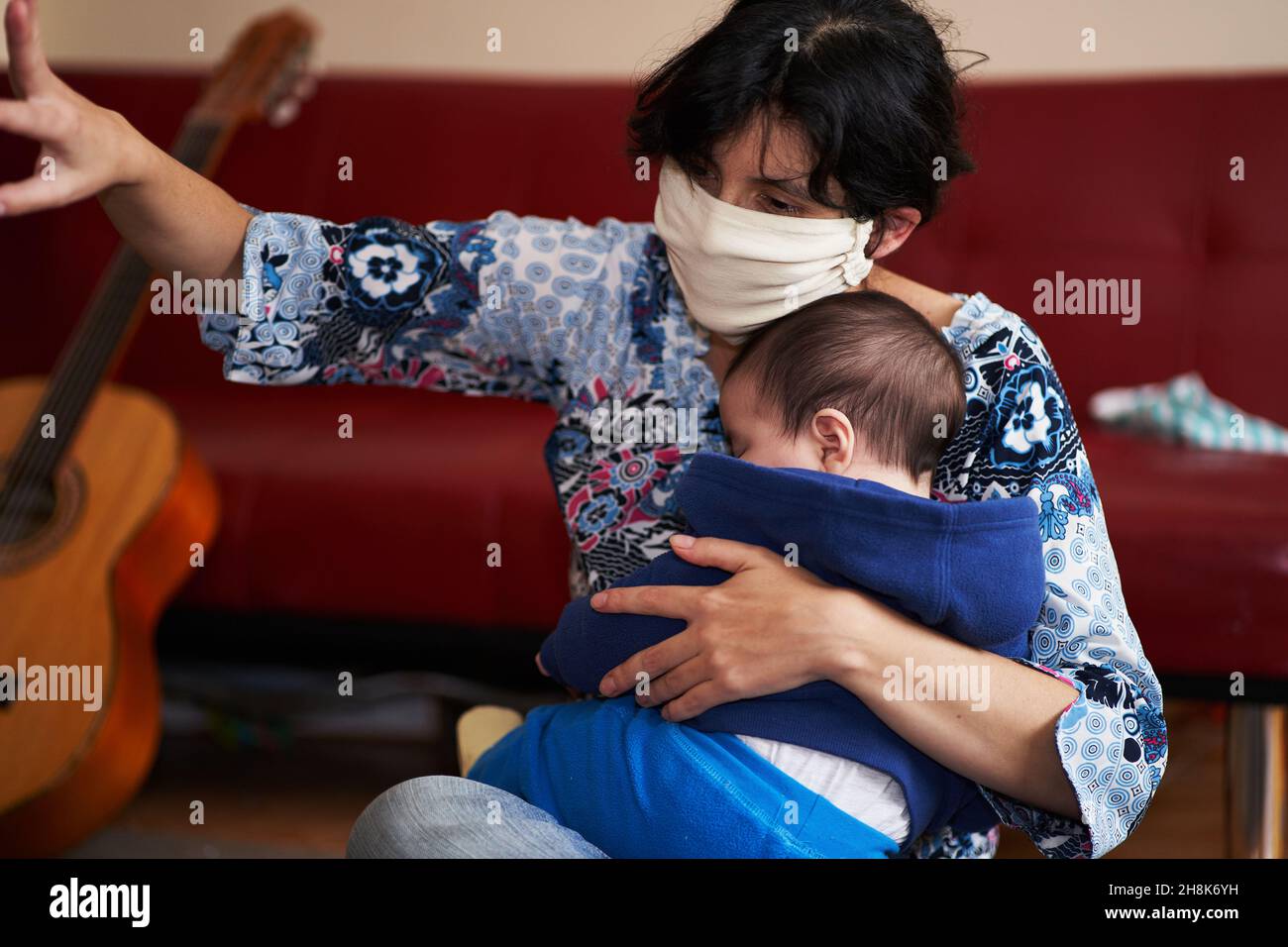 donna con una maschera tiene un bambino nelle sue braccia mentre gioca puntando alle cose. volto stanco. covid-19 coronavirus Foto Stock