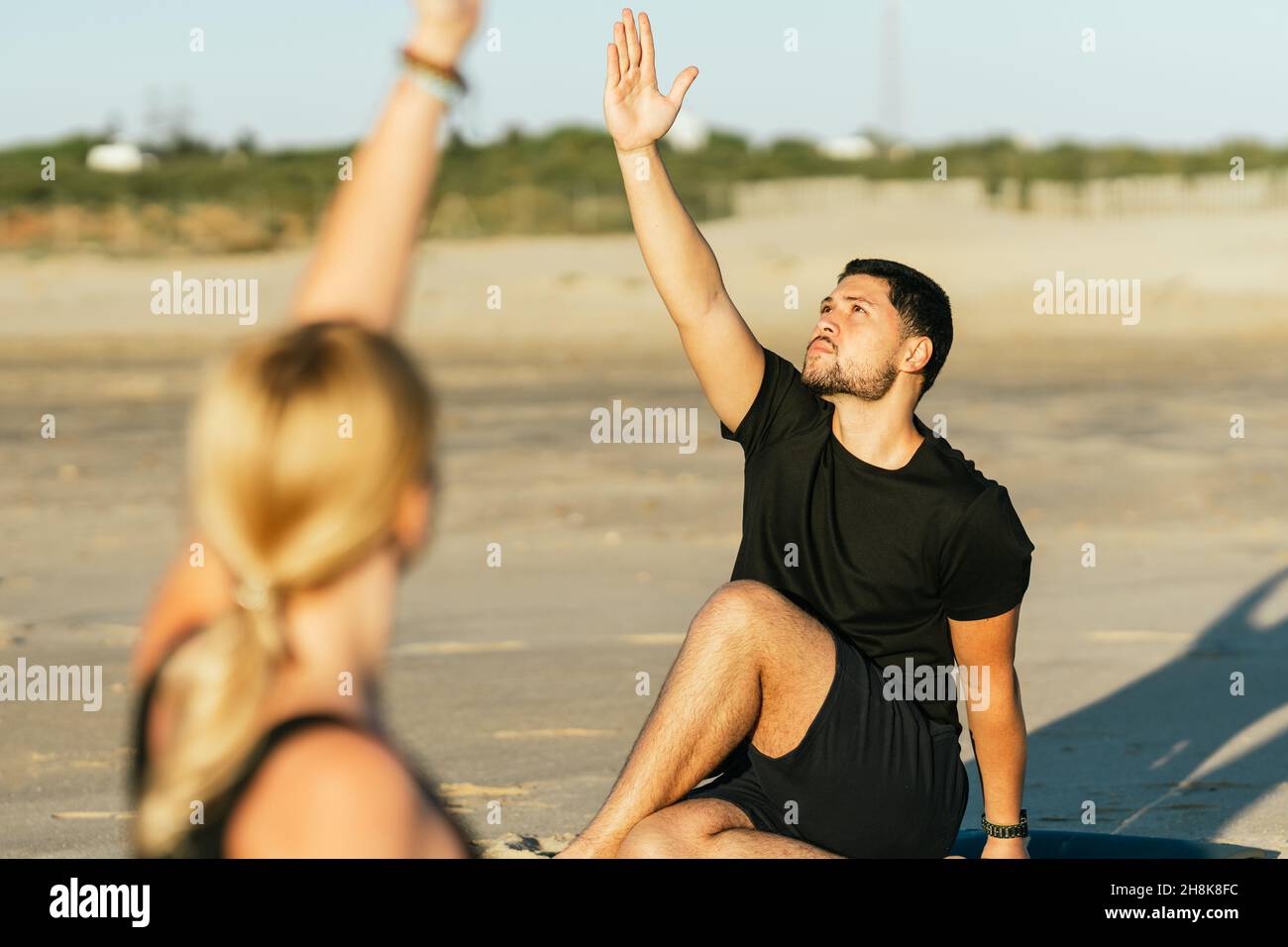 Uomo raisin braccio mentre fare uno yoga accanto al suo allenatore sulla spiaggia Foto Stock