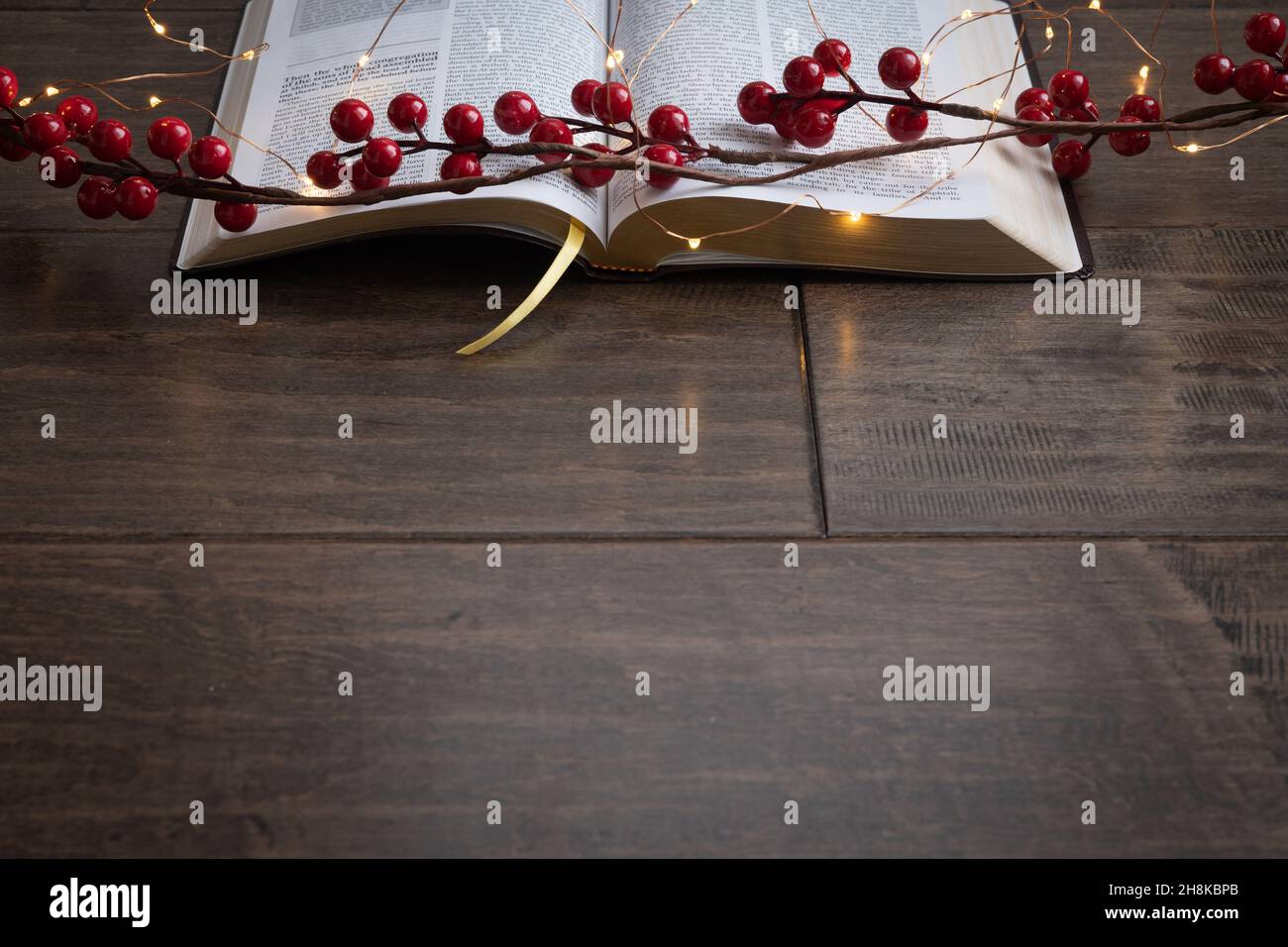 Rosso bacche ghirlanda e stringa di mini fata luci di natale su una bibbia aperta su uno sfondo di legno scuro con spazio copia Foto Stock