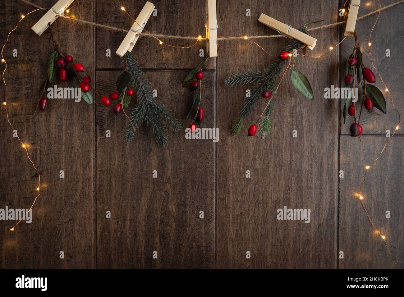 Cornice natalizia con rametti di rami con foglie verdi e bacche rosse appese ad un vestito con spilli di legno scuro Foto Stock