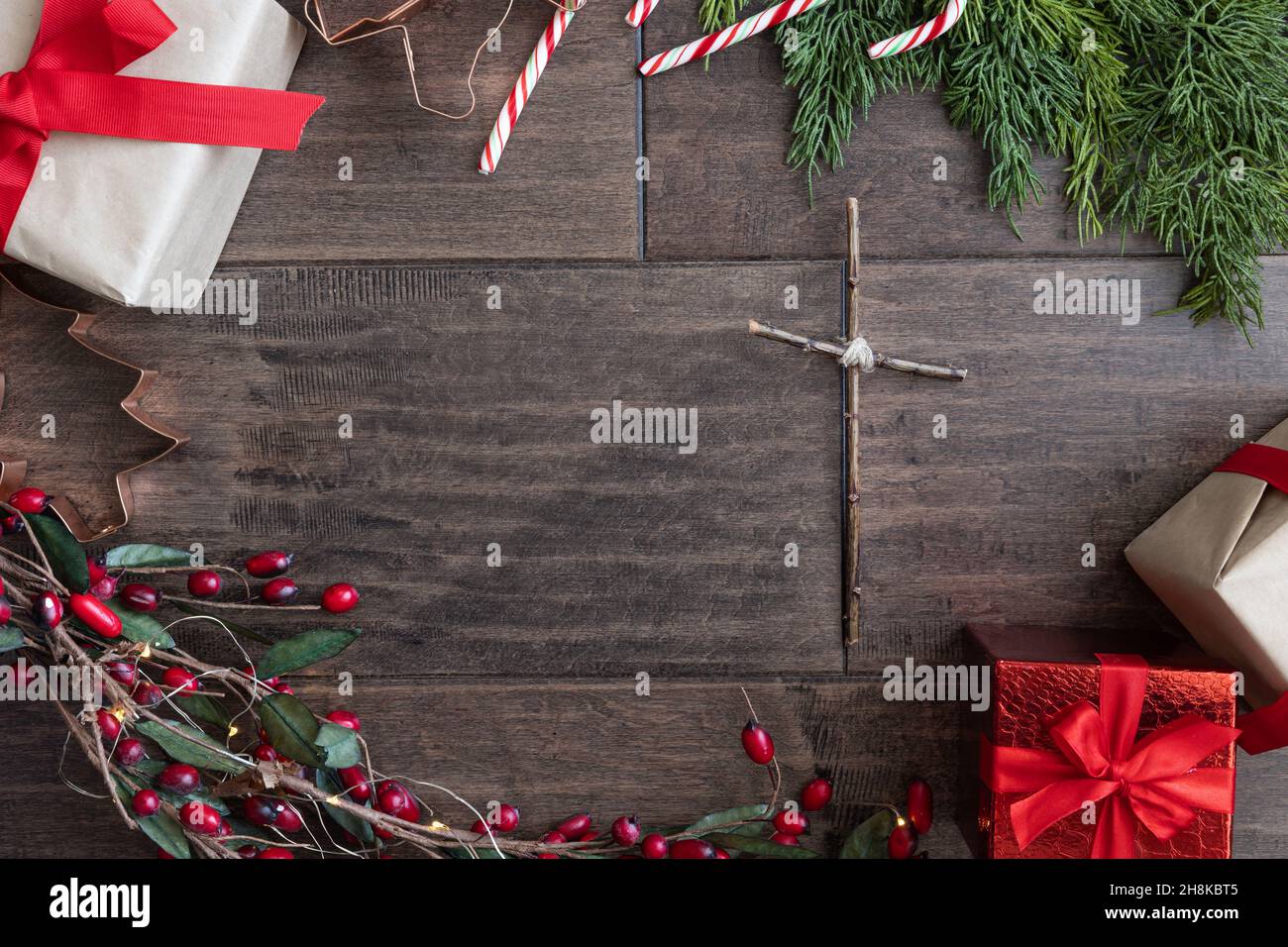 Cornice natalizia del presente, caramelle, bughs sempreverdi in rosso e verde con una semplice croce cristiana con spazio copia su sfondo di legno scuro Foto Stock