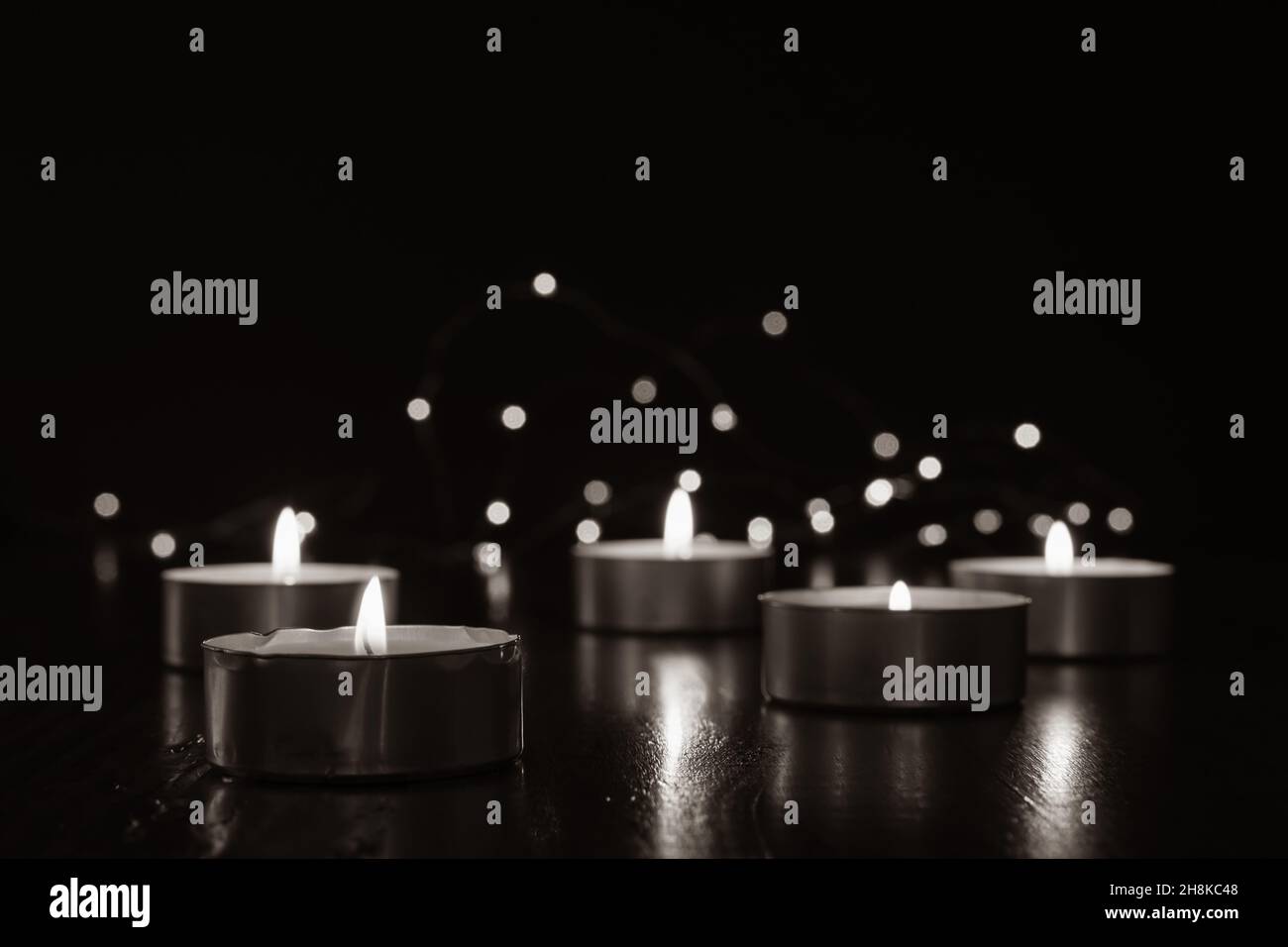Mini candele di luce del tè che bruciano al buio con luci fairy e fiamma che si riflette su di tavola di legno scuro con spazio copia Foto Stock
