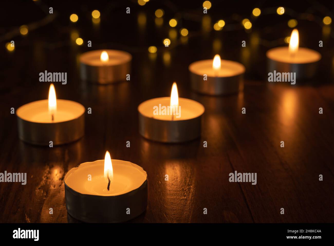 Mini candele di luce del tè che bruciano al buio con luci fairy e fiamma che si riflette su di tavola di legno scuro con spazio copia Foto Stock