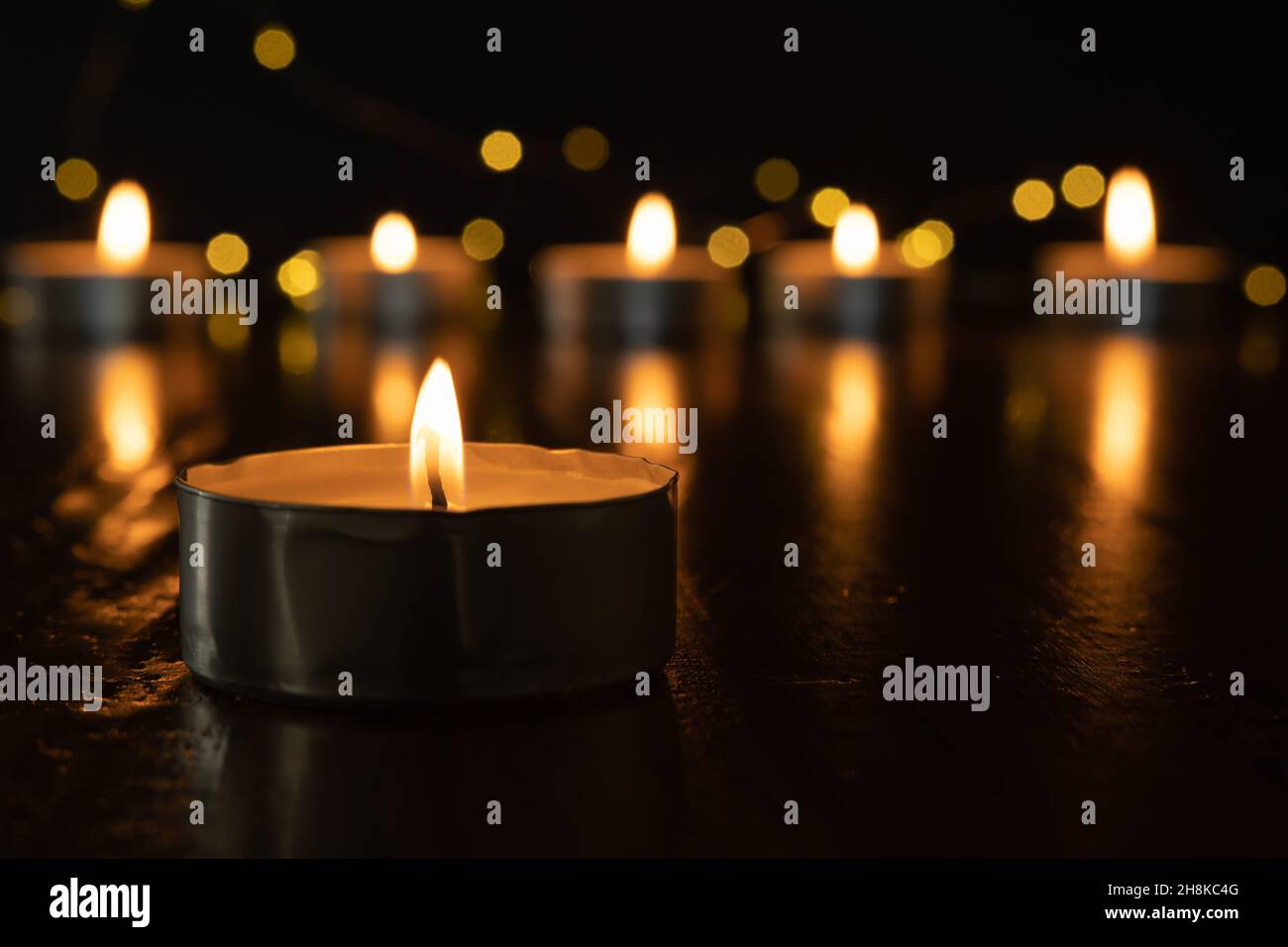 Mini candele di luce del tè che bruciano al buio con luci fairy e fiamma che si riflette su di tavola di legno scuro con spazio copia Foto Stock