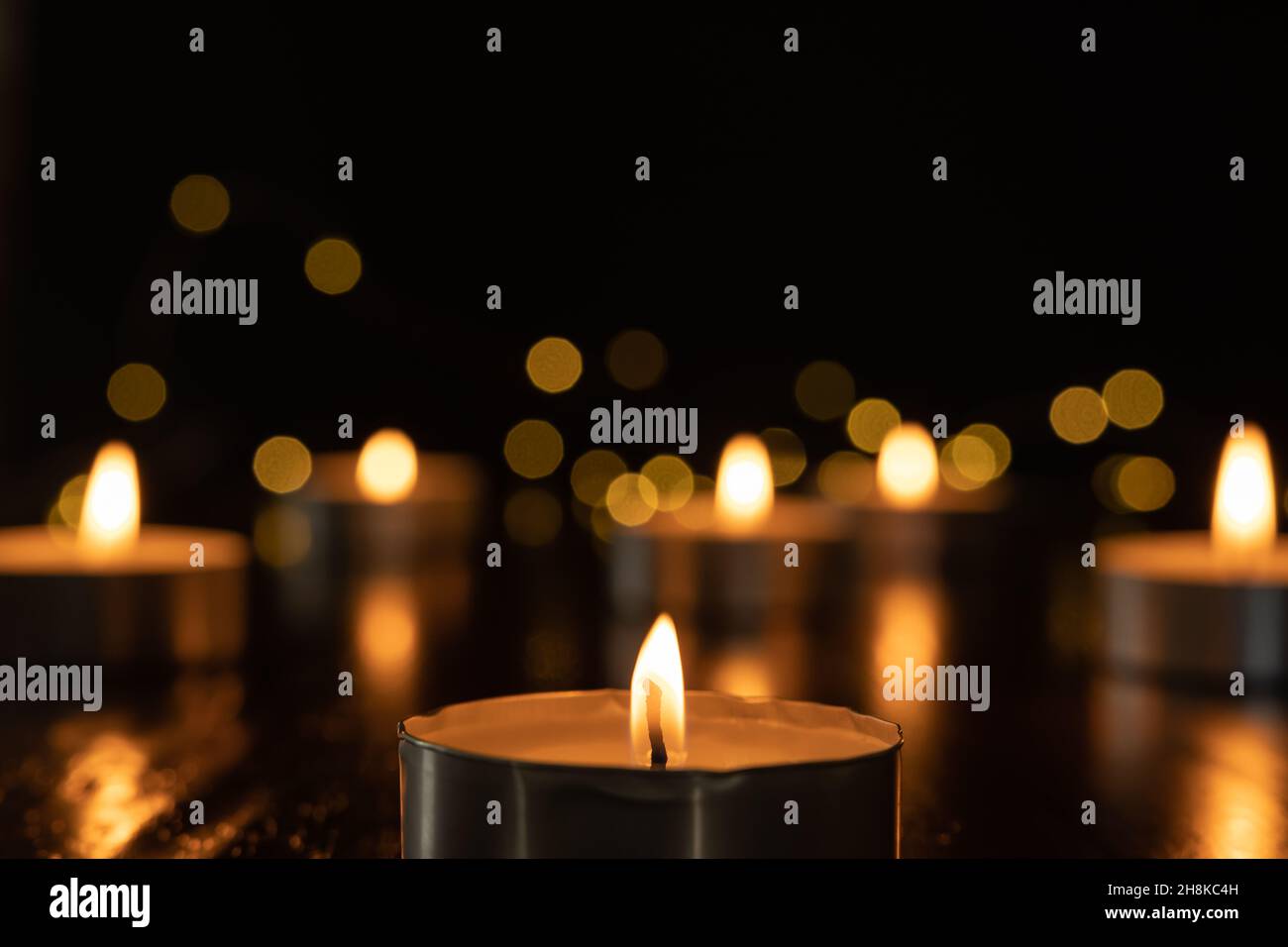 Mini candele di luce del tè che bruciano al buio con luci fairy e fiamma che si riflette su di tavola di legno scuro con spazio copia Foto Stock