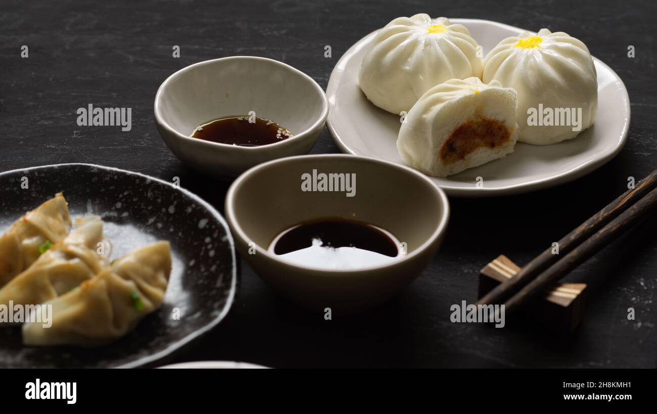Panini di maiale e gnocchi cinesi al vapore con salsa di soia e salsa di soia dolce su un tavolo nero. Cucina asiatica. Foto Stock