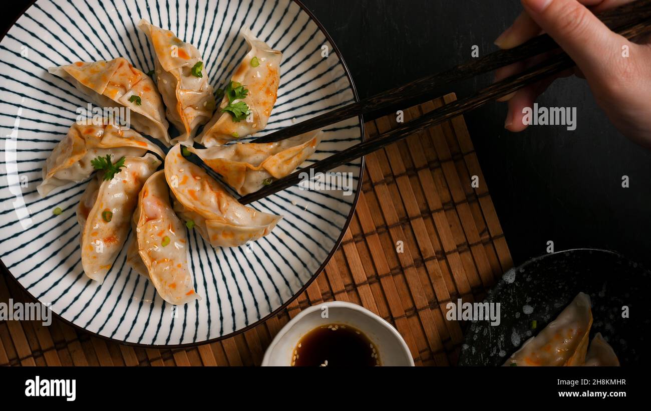 Vista dall'alto, primo piano le mani di una donna usano bacchette con gnocchi di gyoza giapponese a vapore. Cucina asiatica. Foto Stock
