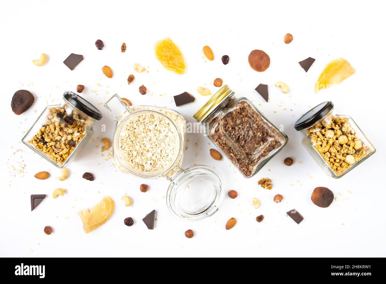 Vista dall'alto di vasetti pieni di avena e vari granoli croccanti con ingredienti sparsi intorno - frutta secca, noci e barrette di cioccolato. Salute mangiare con Foto Stock