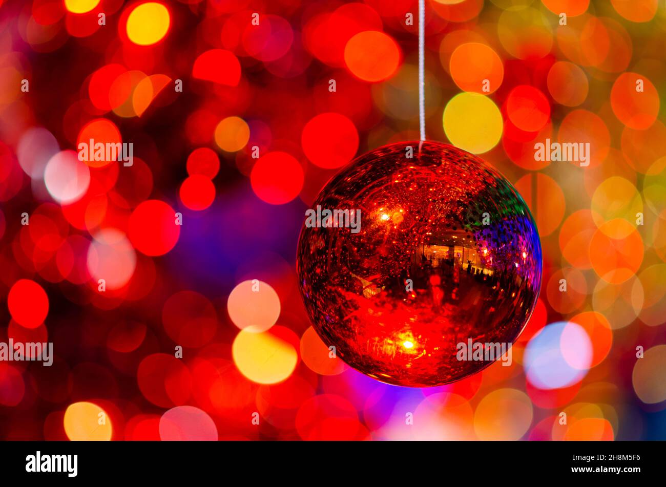 Bauble rosso appeso a decorare per le vacanze di Natale con bokeh colorato dalla luce e altri baubles. Foto Stock