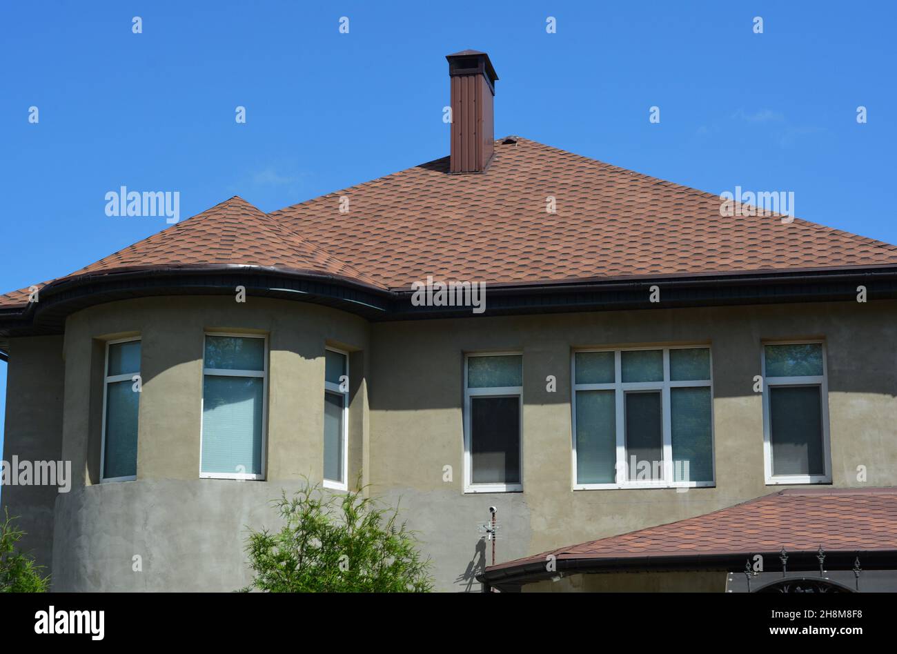 Una casa incompleta in costruzione con una parete semicircolare in stucco intonacata con finestre a bovindo, e il tetto coperto con tegole da copertura in asfalto Foto Stock