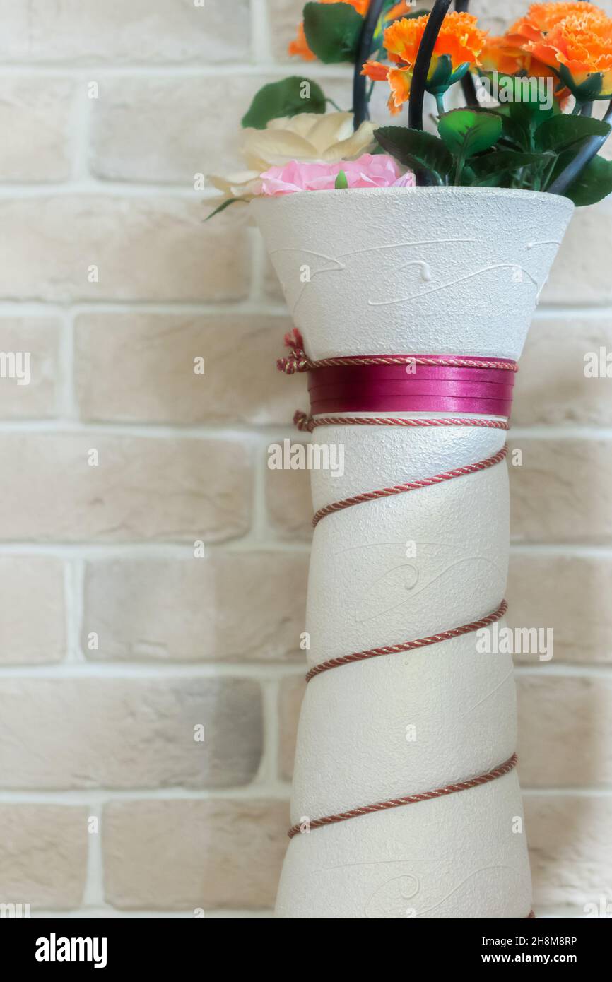 Alto vaso in ceramica con fiori artificiali vicino a una parete in mattoni in stile loft Foto Stock