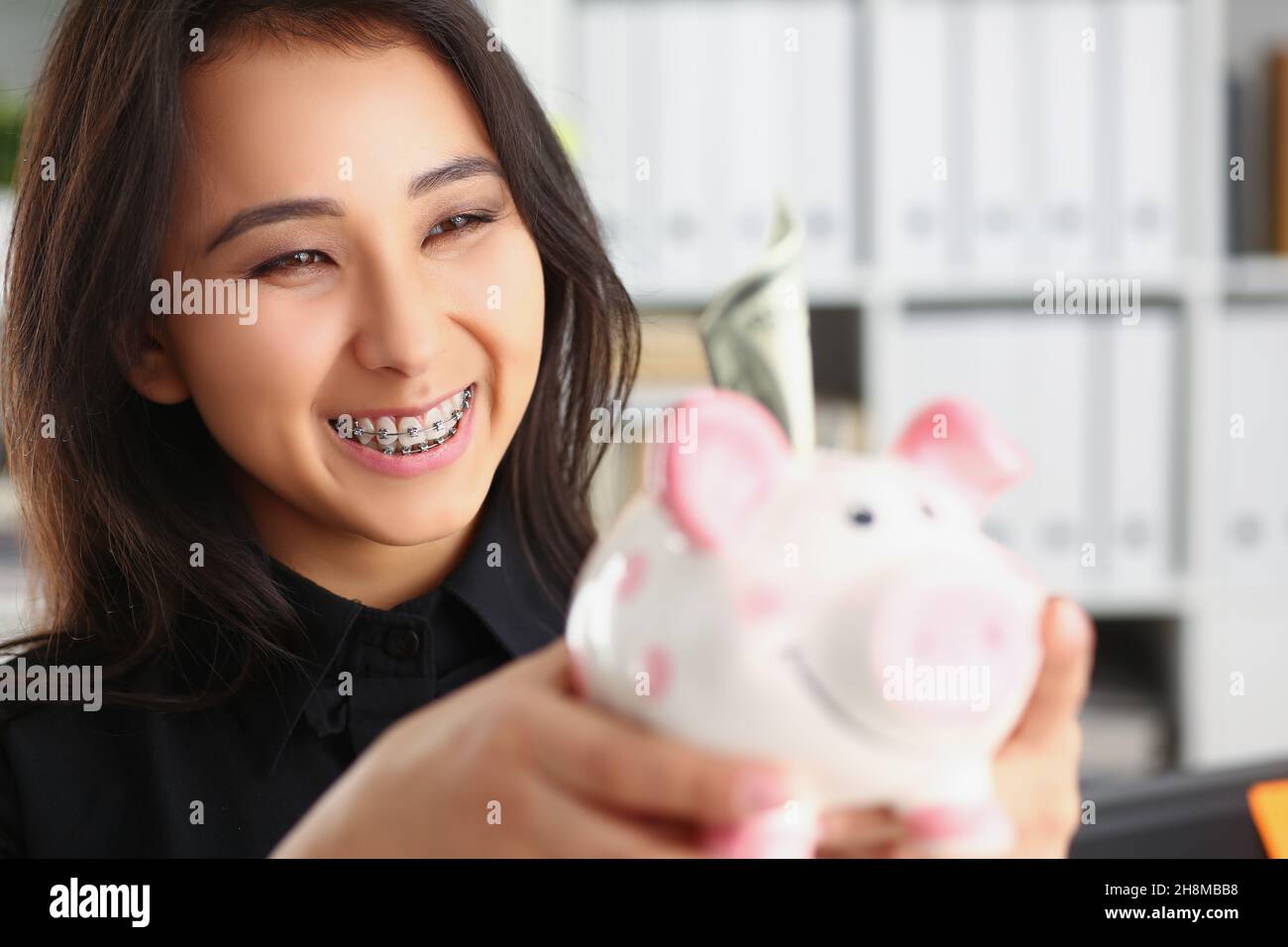 Bella ridendo giovane donna che tiene piggybank con banconota in esso Foto Stock