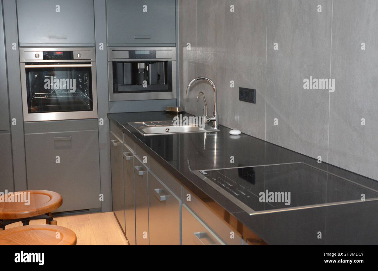 Un moderno design interno della cucina con un piano cottura nero con un lavello  e un piano cottura elettrico, armadi grigi, un forno incorporato e una  macchina per il caffè Foto stock -