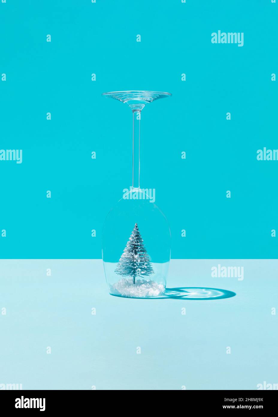 Albero di Natale nella neve all'interno di un bicchiere di vino su sfondo blu. Concetto minimo Foto Stock