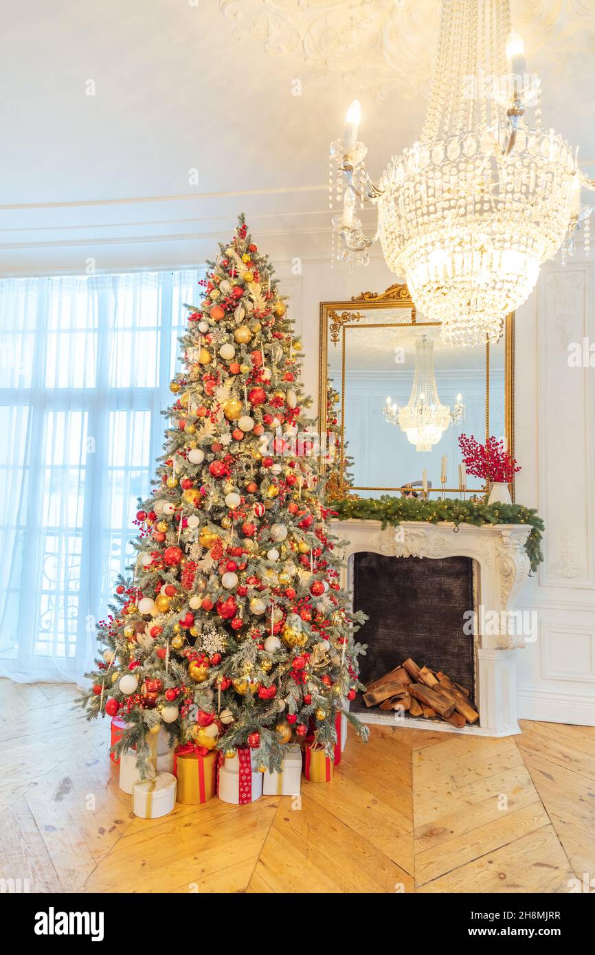 Camera interna decorata in stile classico natalizio, albero di Capodanno con  decorazioni rosse e dorate. Moderno appartamento di design in stile  classico bianco con camino e albero di Natale. Vigilia di Natale