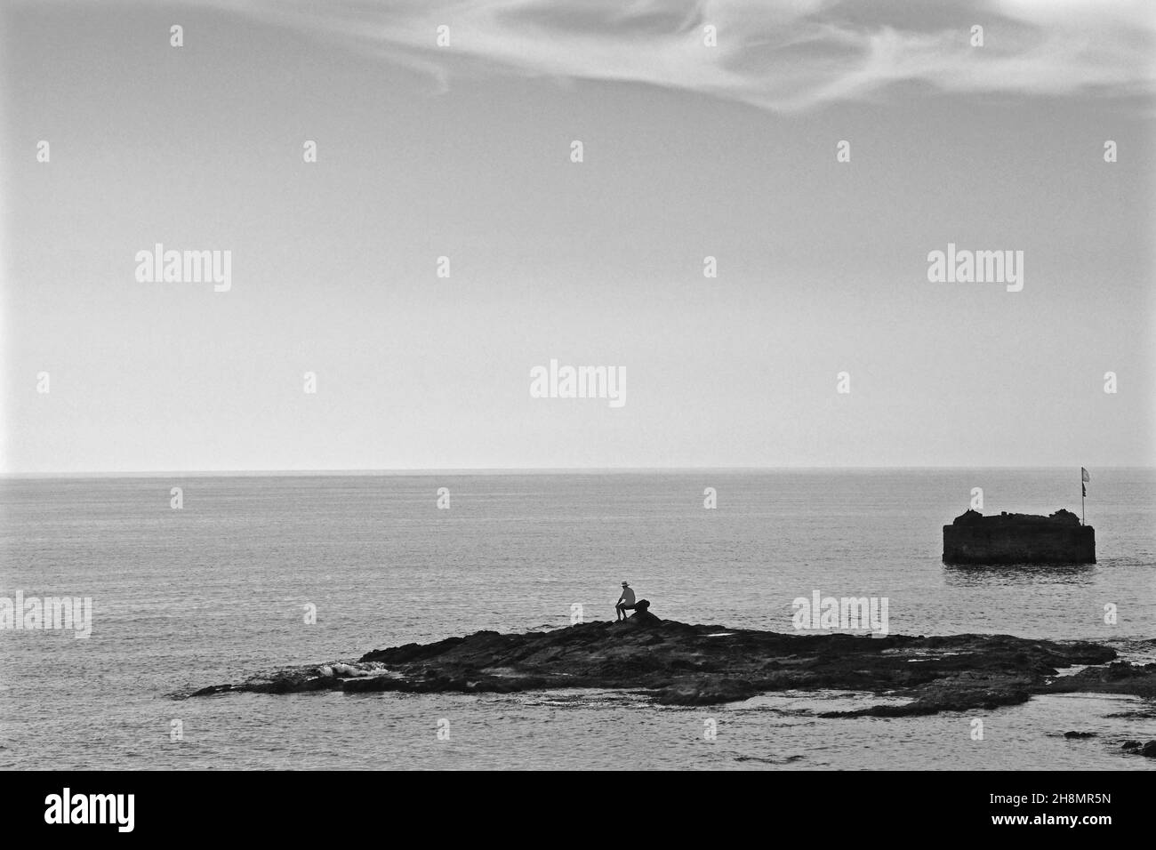 Uomo seduto da solo su piccola isola rocciosa, isola rocciosa, uomo al mare, solitudine, pensierosità, sindrome di Robinson, sensazione di Robinson, Villaricos Foto Stock