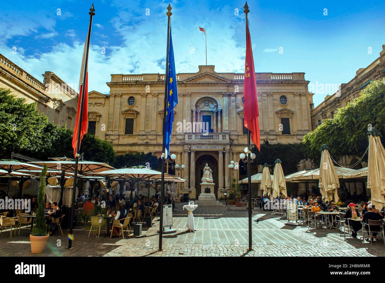 Vista dell'edificio della Biblioteca Nazionale di Malta, di fronte alla scultura in marmo della Regina Vittoria, nel flagpole in primo piano, sul lato dei turisti in Foto Stock
